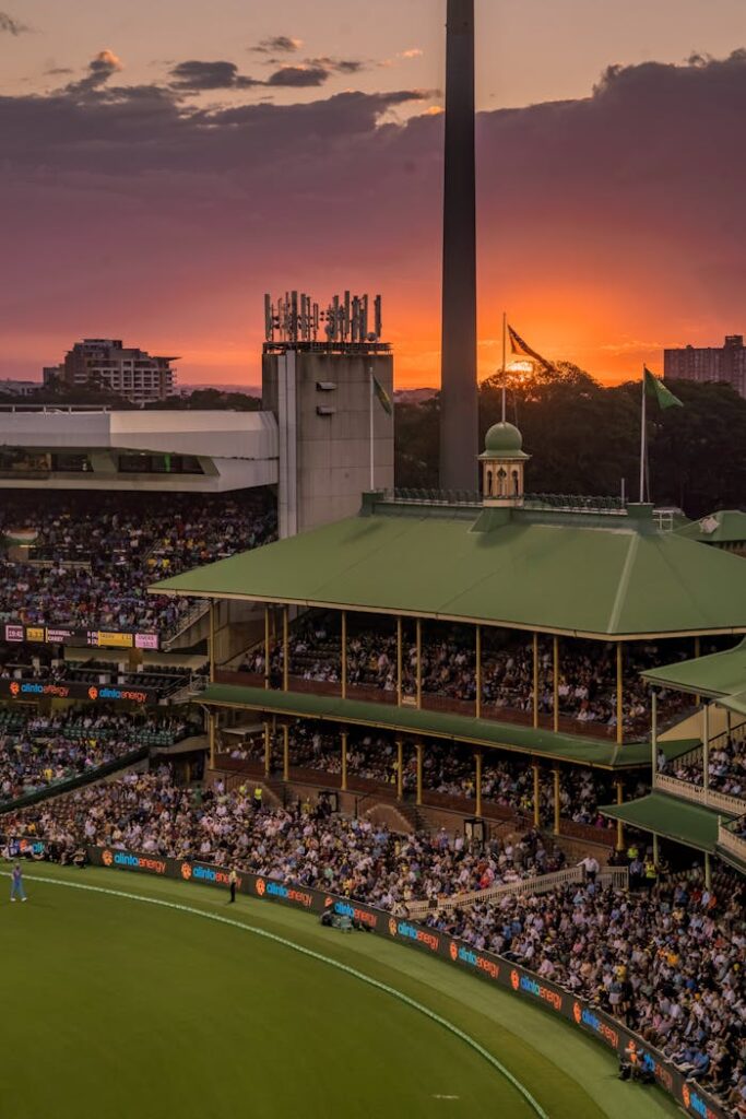 A colorful sunset over a bustling cricket stadium, capturing the lively atmosphere of the event.